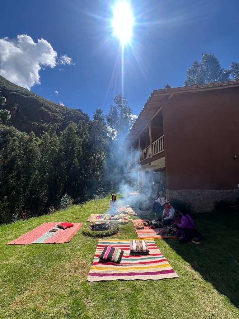 People seated on colorful blankets around a small fire on the lawn beside the house