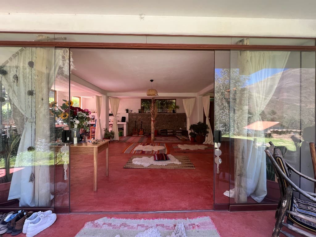 Open glass doors leading into the gathering room with woven rugs, flowers, and mountain light
