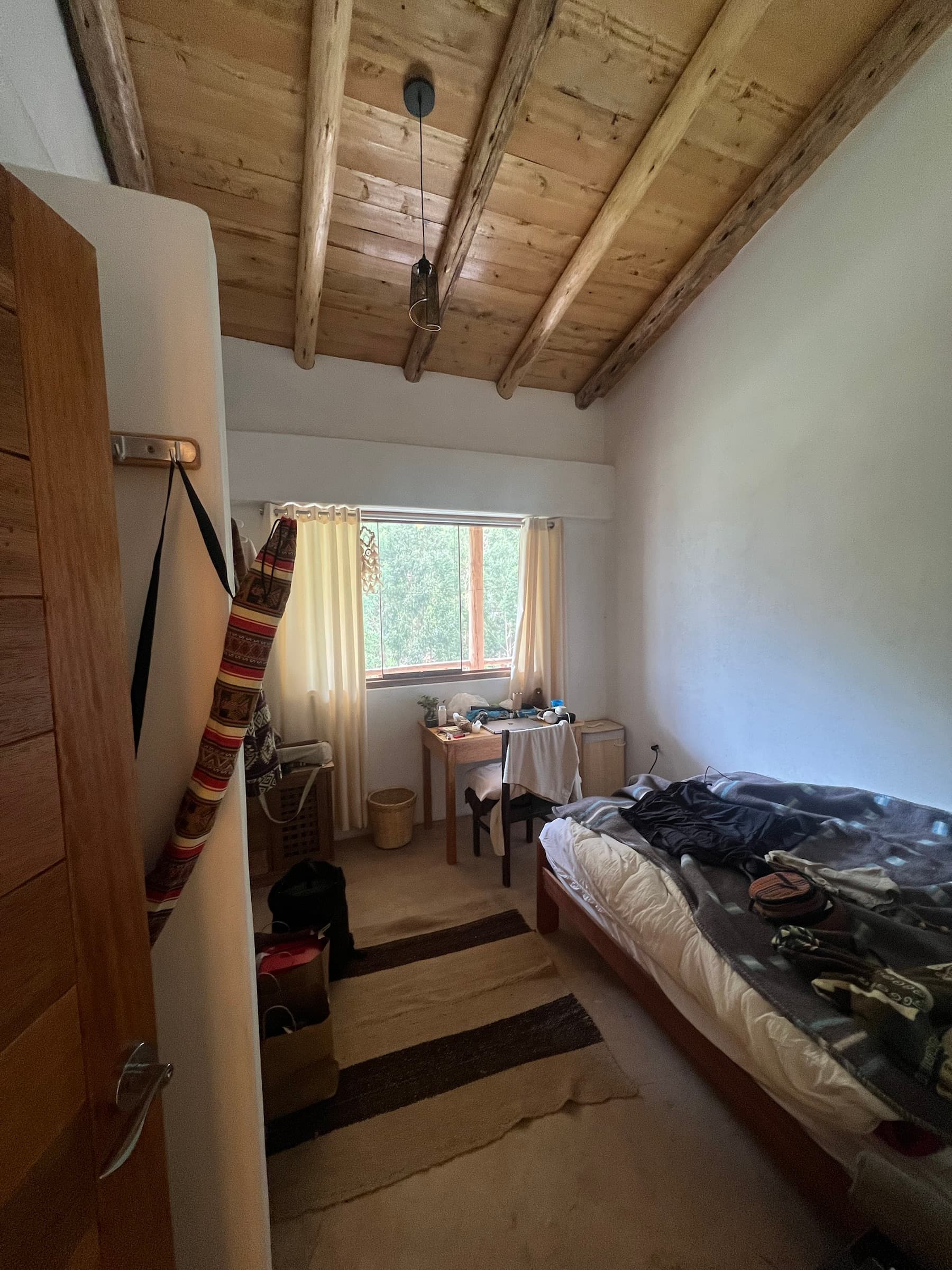 Simple guest room with a high wooden ceiling and a window overlooking trees
