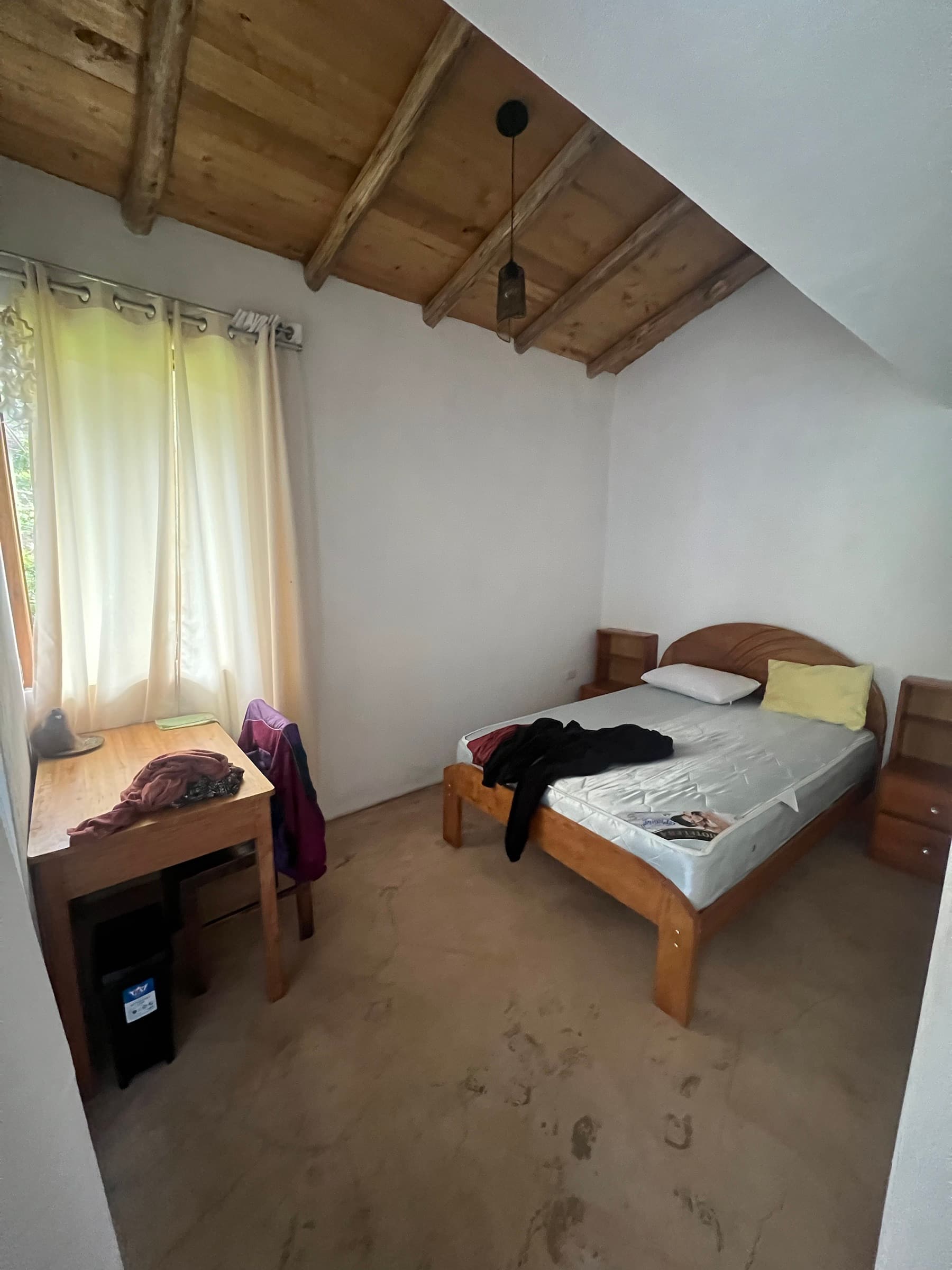 Compact bedroom with a single bed, side table, and desk by the window