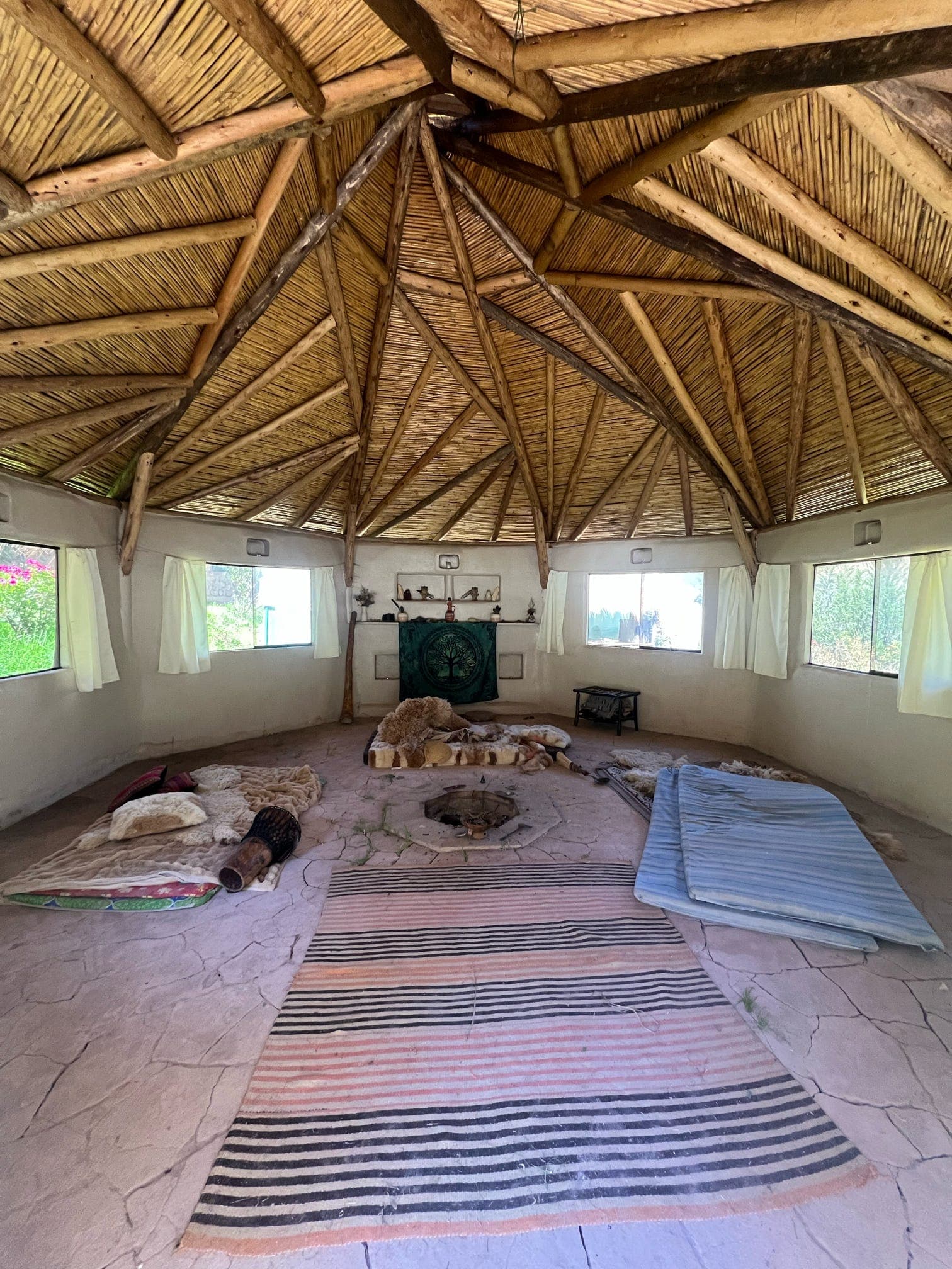Circular gathering room with a thatched wooden ceiling, rugs on the floor, and windows around the walls