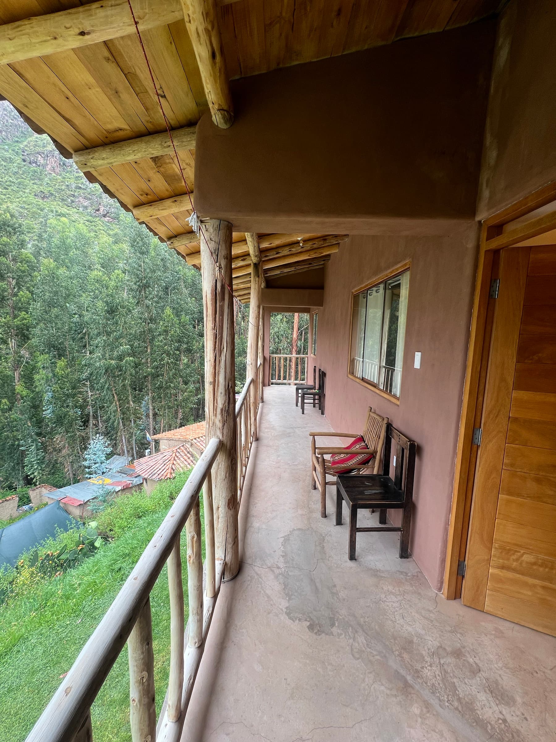 Covered wooden balcony overlooking trees and the hillside beside the house