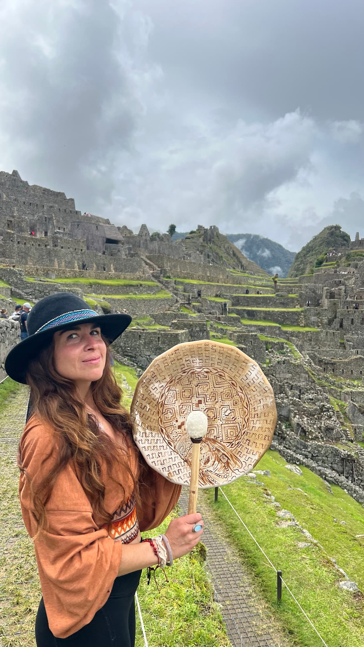 Daniella standing at Machu Picchu holding a woven ceremonial fan