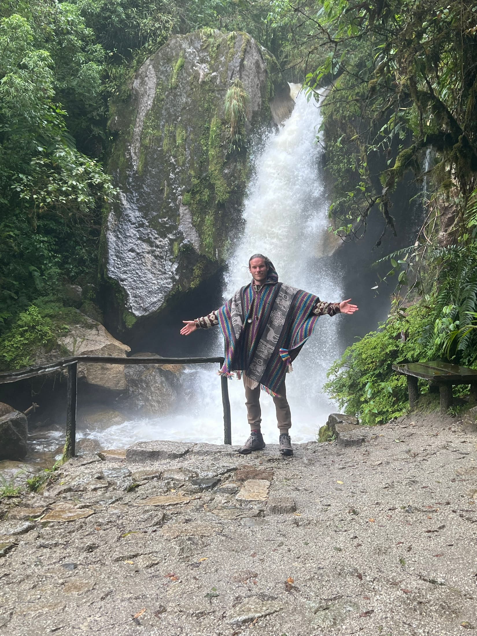 David standing with open arms in front of a waterfall in lush greenery